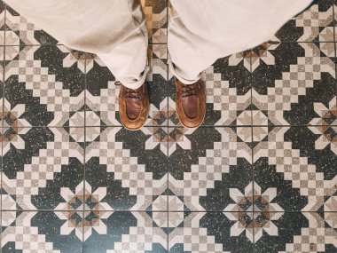 Kişi desenli bir zeminde duruyor, klasik geometrik beton fayansları sergiliyor.