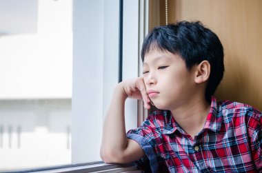 Üzgün çocuk pencereden dışarı bakıyor