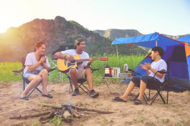 Genç Asyalı bir aile kamp alanında gitarla şarkı söylüyor, anne ve babası açık bir çadırda kamp yapıyor.. 