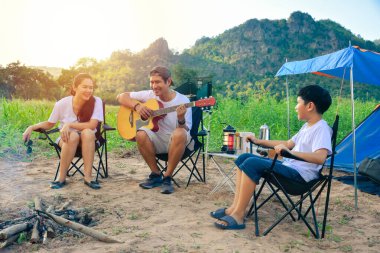 Genç Asyalı bir aile kamp alanında gitarla şarkı söylüyor, anne ve babası açık bir çadırda kamp yapıyor.. 
