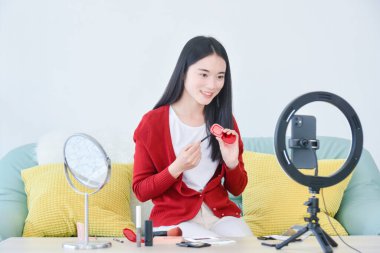 Genç Asyalı kadın makyaj sanatçısı, güzellik vlogcusu veya blogcu akıllı telefonla kozmetik makyaj öğretim videosu kaydediyor, sosyal medyada canlı internet paylaşımı.
