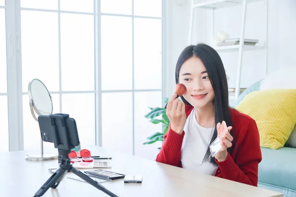 Young Asian female makeup artist , beauty vlogger or blogger recording  cosmetic makeup tutorial vlog by smart phone ,share on social media live streaming Internet.