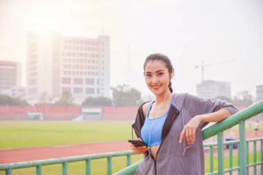 Spor kıyafetli güzel bir Asyalı kadın şehirde egzersiz yaptıktan sonra kulaklıkla müzik dinliyor..