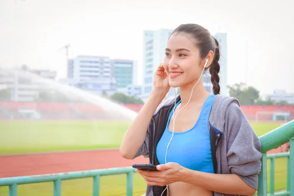 スポーツウェアの美しいアジアの女性は 市内で屋外で運動した後 イヤホンで音楽を聴く — ストック写真