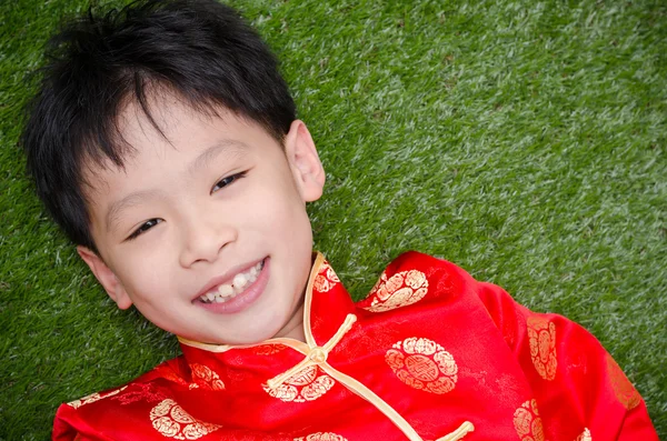 Jongen in Chinees kostuum liggend op grasveld — Stockfoto