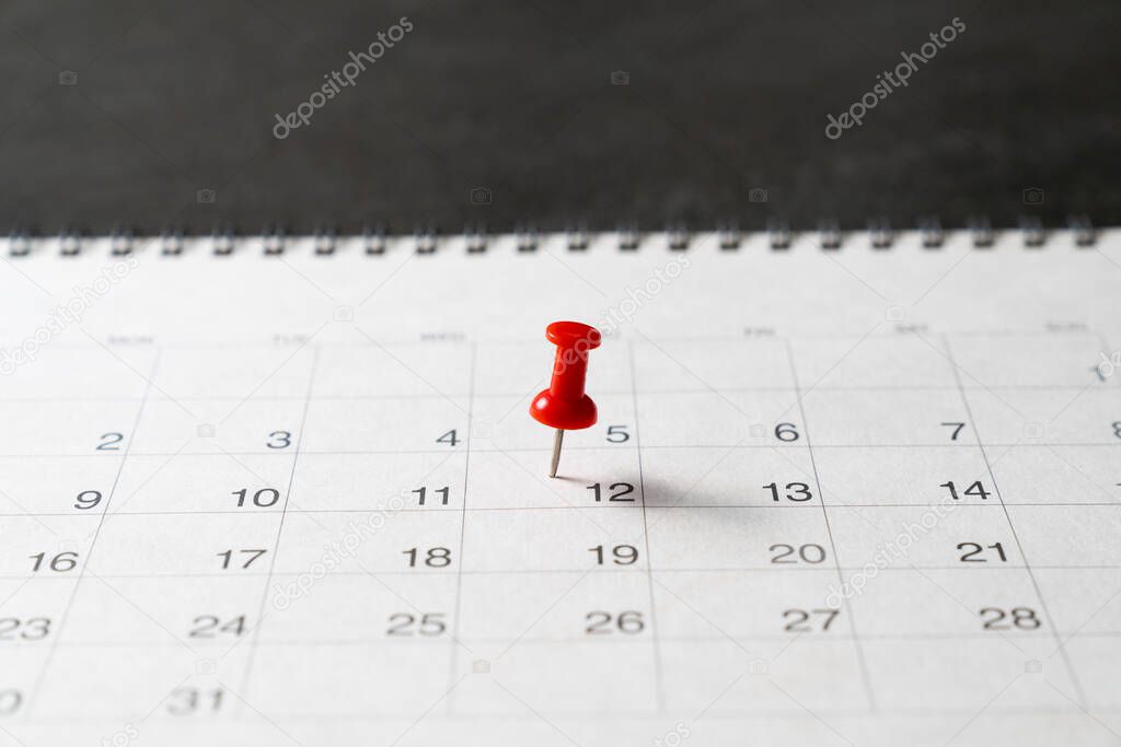 close up of red pin on calendar on black table background, planning for business meeting or travel planning concept