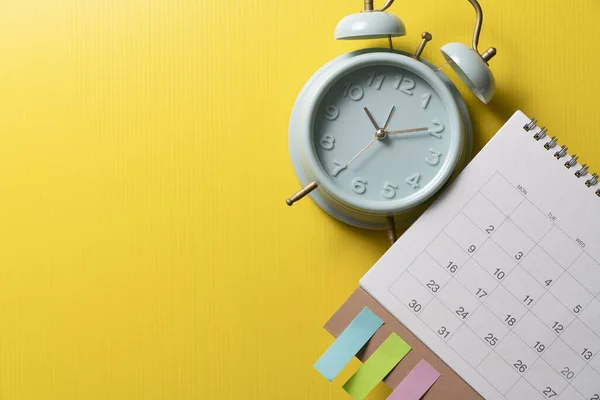 close up of alarm clock and calendar on the yellow table background, planning for business meeting or travel planning concept