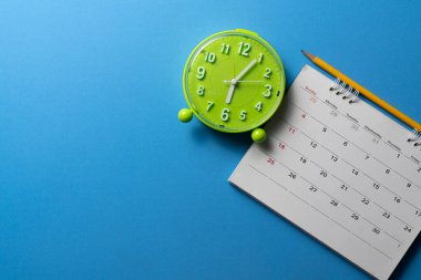 mavi masa arka planında takvim, kalem ve alarmın kapatılması, iş toplantısı veya seyahat planlama konsepti