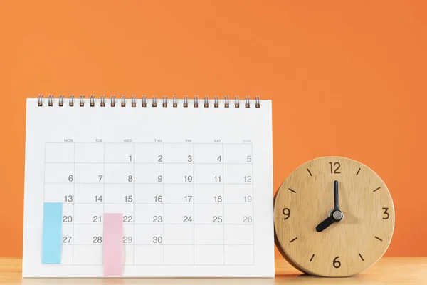 close up of calendar and alarm clock on the table with orange background, planning for business meeting or travel planning concept