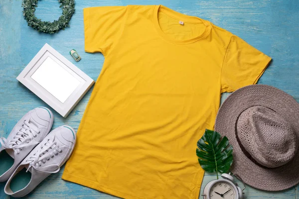 Mockup of a yellow t-shirt blank shirt template with accessories on the wooden table background, lifestyle and travel concept