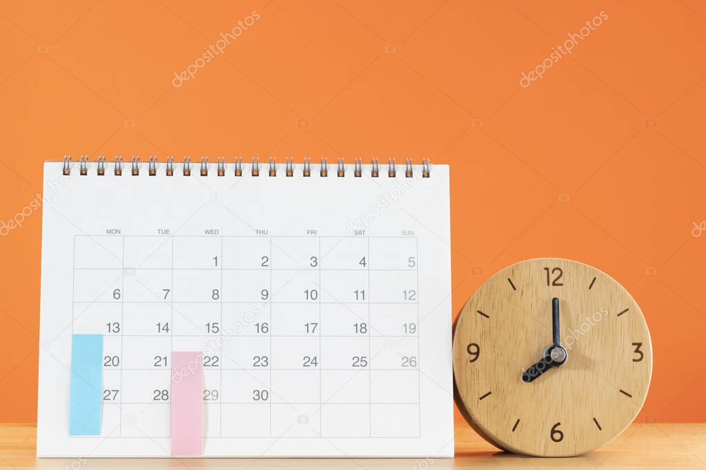 close up of calendar and alarm clock on the table with orange background, planning for business meeting or travel planning concept