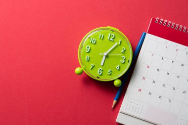 Kırmızı masa arkaplanındaki takvim ve alarmın kapatılması, iş toplantısı ya da seyahat planlama konsepti