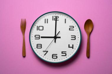 Yemek kaşığı ve çatal, pembe arka planda sağlıklı kahvaltı konsepti.