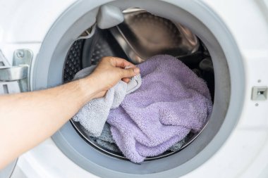 Kirli çamaşırları modern bir çamaşır makinesine yükleyen bir elin yakın çekimi. Çamaşır günü konsepti ve ev işleri