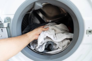 Kirli çamaşırları modern bir çamaşır makinesine yükleyen bir elin yakın çekimi. Çamaşır günü konsepti ve ev işleri