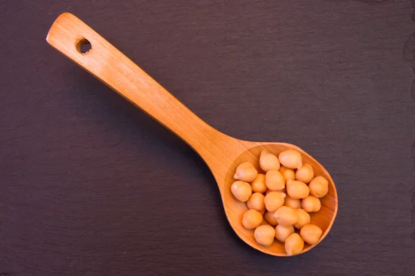 Garbanzos cocidos en una cuchara de madera en pizarra vista desde arriba — Foto de Stock