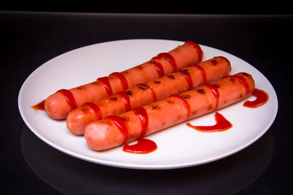 Sausages with tomato sauce on black — Stock Photo, Image