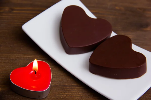 Candle and chocolates in a heart shape on wood close — Stock Photo, Image