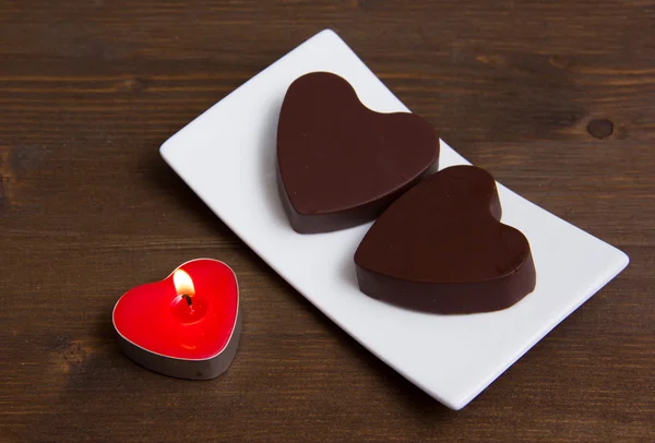 Candle and chocolates in a heart shape on wood — Stock Photo, Image