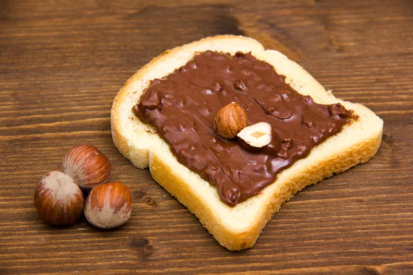 Fatia de pão com chocolate com avelãs em madeira — Fotografia de Stock