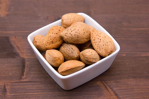 Almendras en cáscara de cuenco cuadrado sobre madera — Foto de Stock