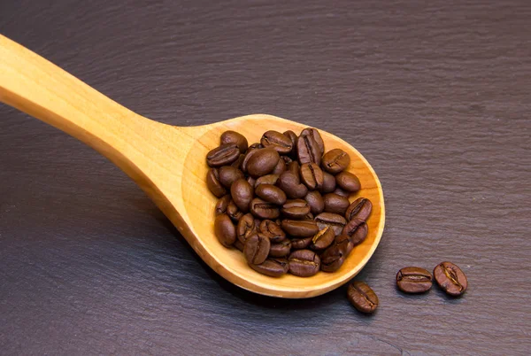 Kávová zrna v dřevěnou lžící na břidlicové horní — Stock fotografie