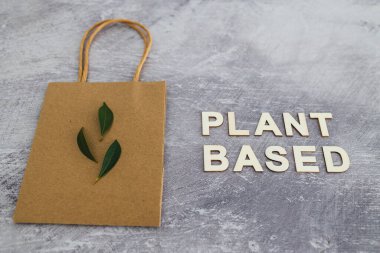 Çevre için sürdürülebilir tüketici seçenekleri, alışveriş torbalı bitki tabanlı metin ve minimalist somut arkaplan üzerindeki yapraklar