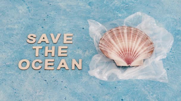 気候変動のために行動し青い背景の海のテキストをビニール袋とカメラのパンニングの上に貝殻で保存 — ストック動画