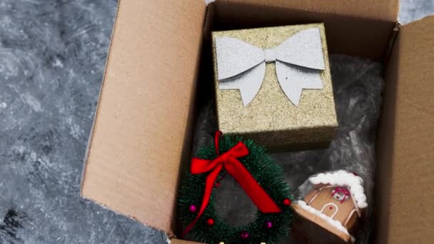 Postpaket mit weihnachtlichen Artikeln darin, darunter funkelndes Geschenk, Kranz und Lebkuchenhaus, Kauf oder Versand von Geschenken online — Stockvideo