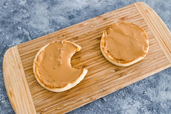 healthy plant-based food recipes concept, English muffins with smooth peanut butter topping on cutting board