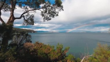 Tazmanya, Avustralya 'daki Tazmanya Sahili' nde el değmemiş vahşi bir manzarayla çevrili gökkuşağı ve fırtınalı gökyüzü.