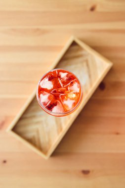 Tahta masanın üzerinde uzun bardakta portakal suyu kokteyli yakındaki pencereden parlayan altın ışık meyveli yaz içecekleri konsepti.