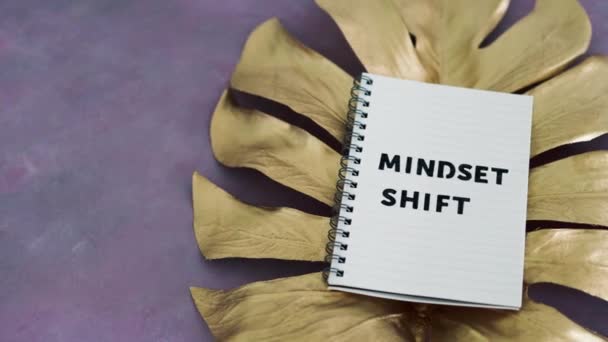 ピンクの背景に金色の葉の上にマインドセットシフトノートパッド 心理学と態度 — ストック動画