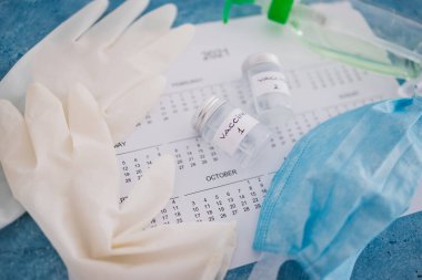 Covid-19 aşısı ve salgına karşı bağışıklık aşısı, Aşı 1 ve Aşı 2 etiketli ampuller 2021 takvimi, eldiven maskesi ve dezenfektanla yan yana.