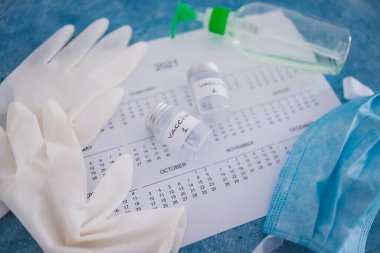 Covid-19 aşısı ve salgına karşı bağışıklık aşısı, Aşı 1 ve Aşı 2 etiketli ampuller 2021 takvimi, eldiven maskesi ve dezenfektanla yan yana.