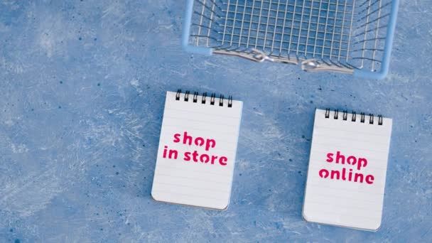 青の背景 競争と小売業界の概念的なイメージ上のノートパッド上の店対ショップオンラインテキストでお店で買い物かご — ストック動画