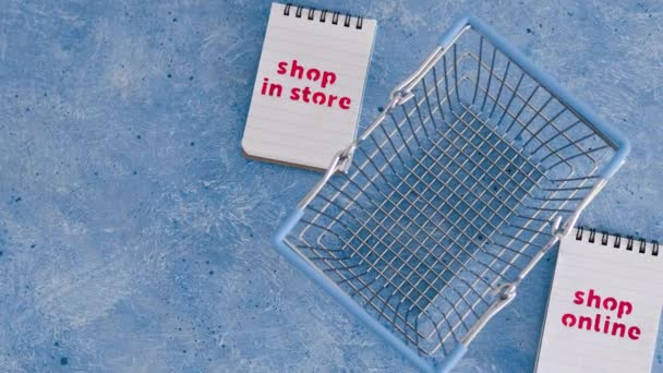 青の背景 競争と小売業界の概念的なイメージ上のノートパッド上の店対ショップオンラインテキストでお店で買い物かご — ストック動画