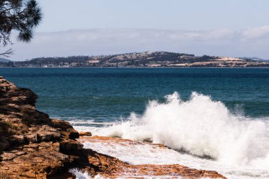 Büyük dalgalar Tazmanya, Avustralya 'da sert rüzgarların estiği bir günde kayalık kıyı şeridine çarpıyor.