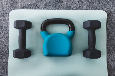 Salonda yoga minderinde kettlebell ve dambıl, spor salonu konsepti ve hafif gri ve mavi tonlarda ağırlık eğitimi. 