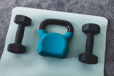 Salonda yoga minderinde kettlebell ve dambıl, spor salonu konsepti ve hafif gri ve mavi tonlarda ağırlık eğitimi. 