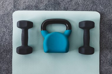 Salonda yoga minderinde kettlebell ve dambıl, spor salonu konsepti ve hafif gri ve mavi tonlarda ağırlık eğitimi. 