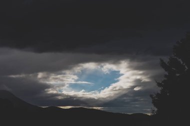 Karanlık, kasvetli, fırtınalı gökyüzü, bulutlar açılıyor ve Tazmanya, Avustralya 'da güneş ışınları ve güneş ışınları parıldıyor.