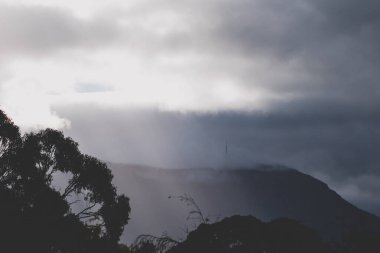 Karanlık, kasvetli, fırtınalı gökyüzü, bulutlar açılıyor ve Tazmanya, Avustralya 'da güneş ışınları ve güneş ışınları parıldıyor.