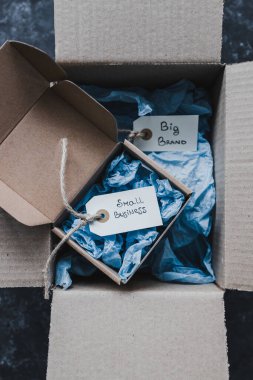 Ürün etiketleri küçük işletmelere karşı büyük ve küçük dağıtım paketlerinin içindeki büyük markalı metinler, müşteri davranışları konsepti ve küçük yerel işletmeleri destekleme