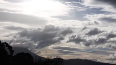 Şiddetli güneş ışınları ile fırtınalı gökyüzünün hızlanması ve bulutların dağların üzerinden yuvarlanması ve kışın Avustralya, Tazmanya 'da yoğun bitki örtüsü çekilmesi