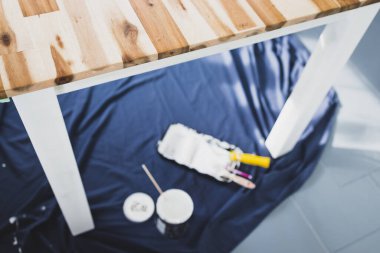 Boya tepsisi silindirli bir tencere beyaz boya ve mavi çarşafın üstünde fırçalar. Tabloyu boyamaya hazır. Boya kutusuyla sığ bir alanda çekilmiş.