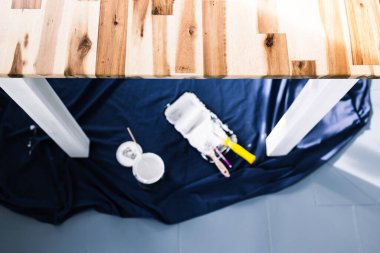 Boya tepsisi silindirli bir tencere beyaz boya ve mavi çarşafın üstünde fırçalar. Tabloyu boyamaya hazır. Boya kutusuyla sığ bir alanda çekilmiş.