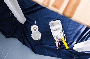 Boya tepsisi silindirli bir tencere beyaz boya ve mavi çarşafın üstünde fırçalar. Tabloyu boyamaya hazır. Boya kutusuyla sığ bir alanda çekilmiş.