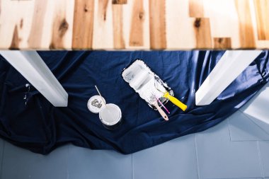 Boya tepsisi silindirli bir tencere beyaz boya ve mavi çarşafın üstünde fırçalar. Tabloyu boyamaya hazır. Boya kutusuyla sığ bir alanda çekilmiş.