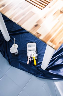 Boya tepsisi silindirli bir tencere beyaz boya ve mavi çarşafın üstünde fırçalar. Tabloyu boyamaya hazır. Boya kutusuyla sığ bir alanda çekilmiş.